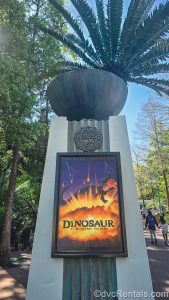 A poster displaying a scary-looking dinosaur and fiery meteorites is affixed to a stone pillar with the symbol for The Dino Institute outside of the DINOSAUR attraction at Animal Kingdom.