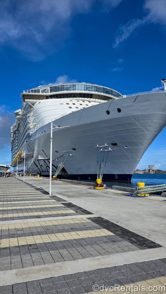 The white exterior of Royal Caribbean’s Wonder of the Seas cruise ship is seen docked in port under a sunny blue sky.