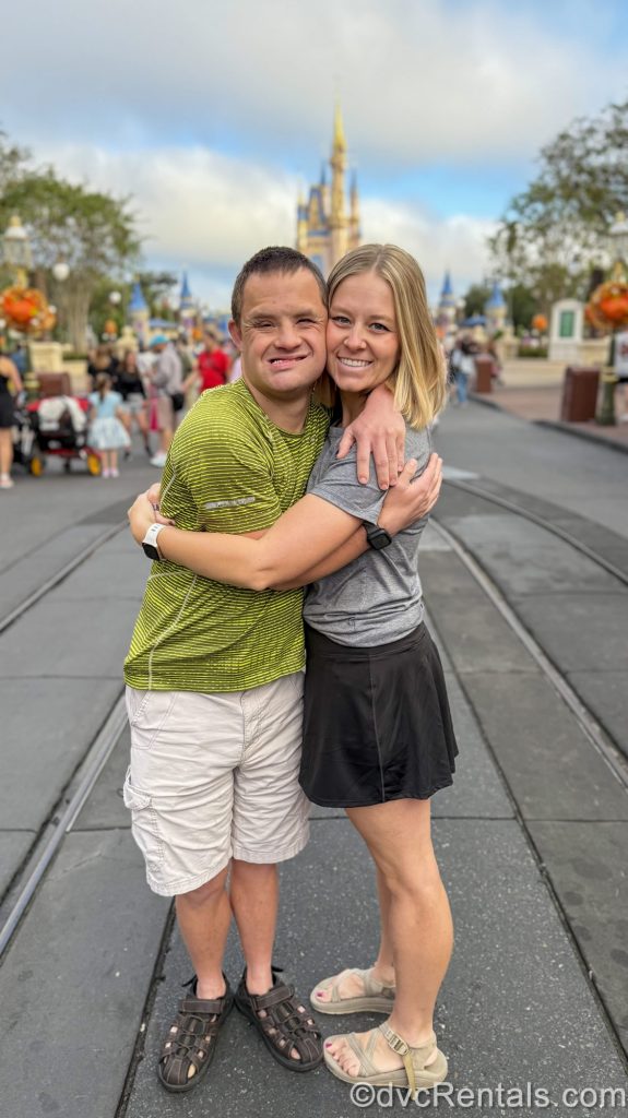 Guest Blogger ErinAdvocates and her brother, Matt, hug and smile while posing together in front of Cinderella Castle at Magic Kingdom under a blue sky.