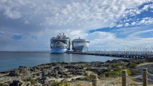 Royal Caribbean’s Wonder of the Seas and Symphony of the Seas cruise ships are docked next to each other at Perfect Day at CocoCay under a sunny sky as guests walk down the pier to enjoy the private island.