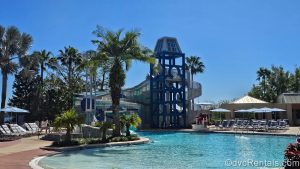 The Mickey tower waterslide at the Bay Cove Pool at Bay Lake Tower at Disney’s Contemporary Resort is seen under a sunny sky behind pool in the foreground.