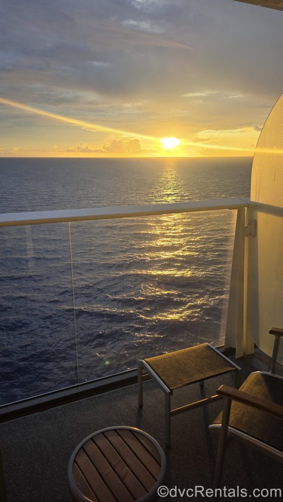The sun illuminates the sky with shades of yellow, orange and blue, as it sets over the ocean horizon, as seen from the stateroom balcony onboard Royal Caribbean’s Wonder of the Seas.