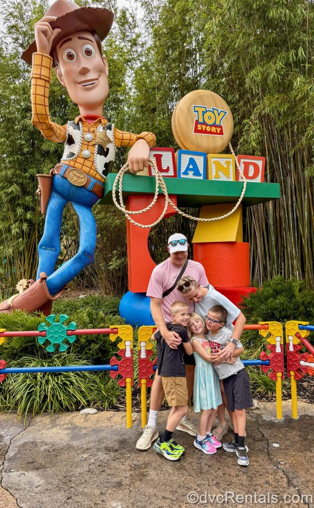 Guest Blogger ErinAdvocates and some of her family pose in a group hug for a photo with Woody and the Toy Story Land sign in the background at Disney’s Hollywood Studios.