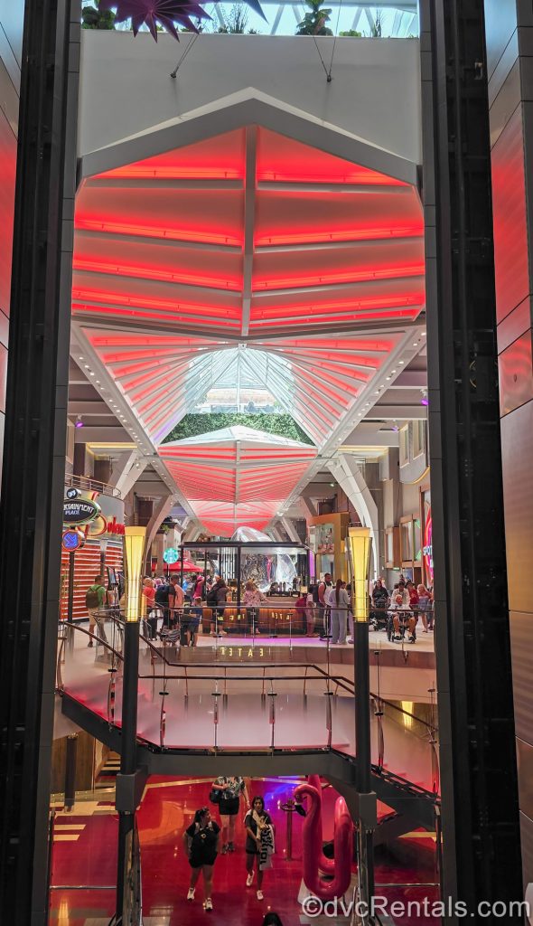 The Royal Promenade on Wonder of the Seas is seen as guests walk up and down the red and white lit space full of shops and dining locations.