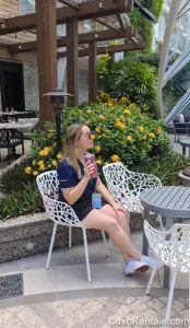 David’s Vacation Club Rentals Team Member Tiffany sits at a table with a drink in the Central Park neighborhood onboard Royal Caribbean’s Wonder of the Seas.