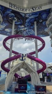 The purple tubes of The Ultimate Abyss slide swirl down from the upper decks under a sign reading “Wonder of the Seas” in navy blue lettering.