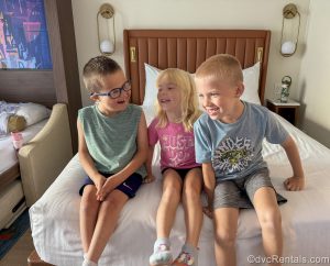 The kids in Guest Blogger ErinAdvocates’ family giggle and smile as they pose for a photo together sitting on the bed in a Two Bedroom Villa at Bay Lake Tower at Disney’s Contemporary Resort.