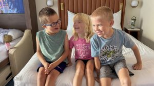 The kids in Guest Blogger ErinAdvocates’ family giggle and smile as they pose for a photo together sitting on the bed in a Two Bedroom Villa at Bay Lake Tower at Disney’s Contemporary Resort.