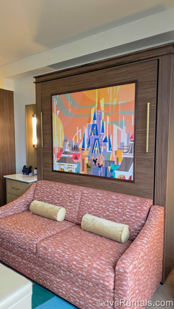 Colorful Mary Blair-style artwork of Cinderella Castle is seen over the sofa in a Two Bedroom Villa at Bay Lake Tower at Disney’s Contemporary Resort.