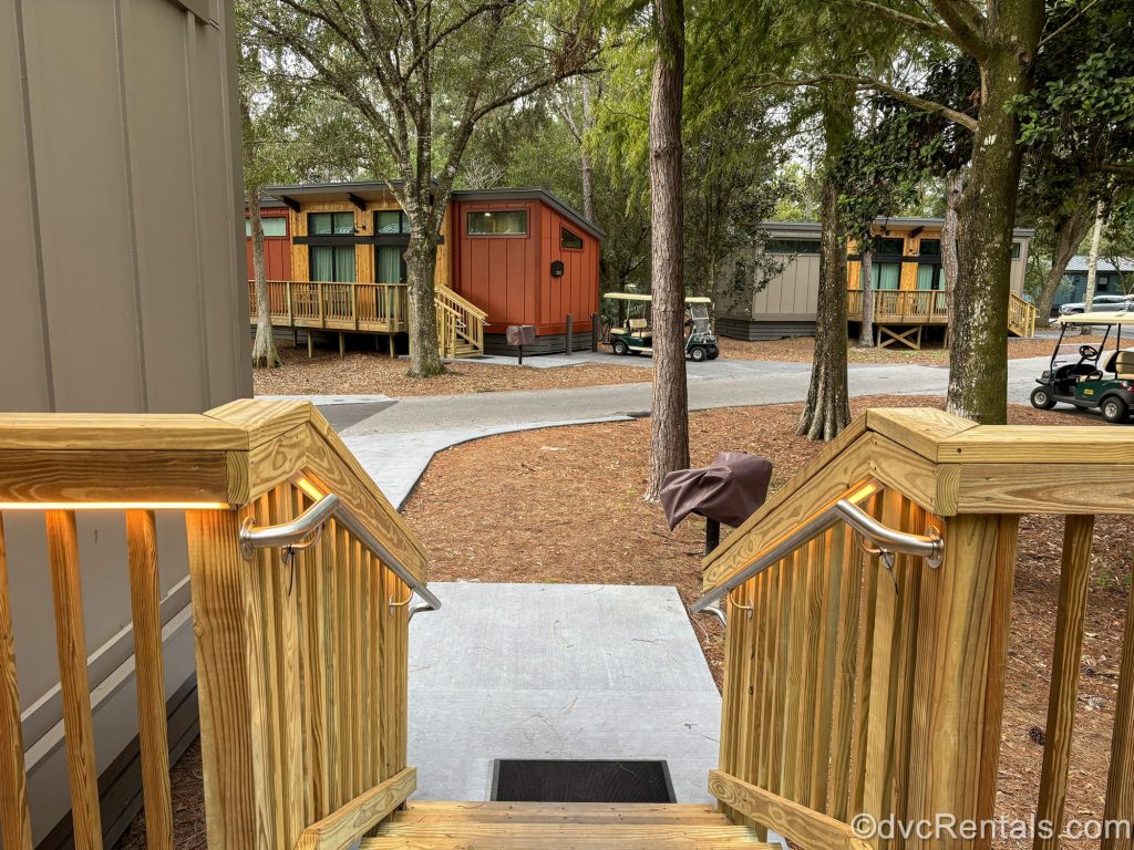 Wooden steps lead down from a One Bedroom DVC Cabin at Disney’s Fort Wilderness Resort. Other cabins, golf carts, and trees are seen in the background.