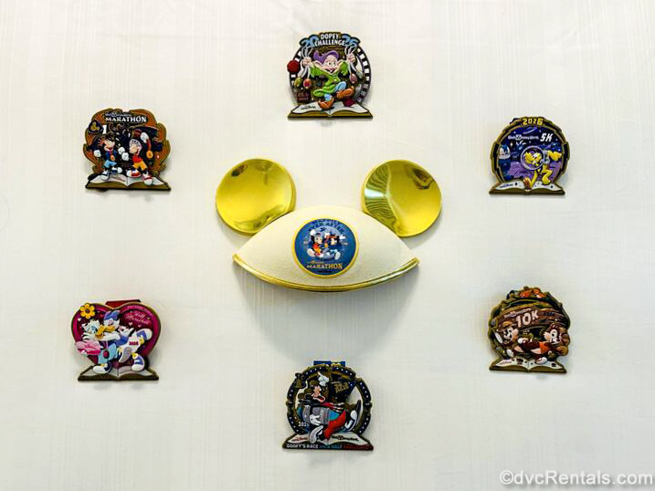 Medals from runDisney races featuring Disney characters are displayed in a circle around a gold Marathon Weekend-themed Mickey Ear hat.