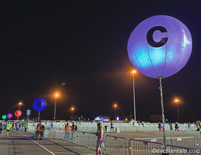 Race participants begin entering their runDisney event locations under a dark night sky as brightly colored circular signs indicate where each corral is.