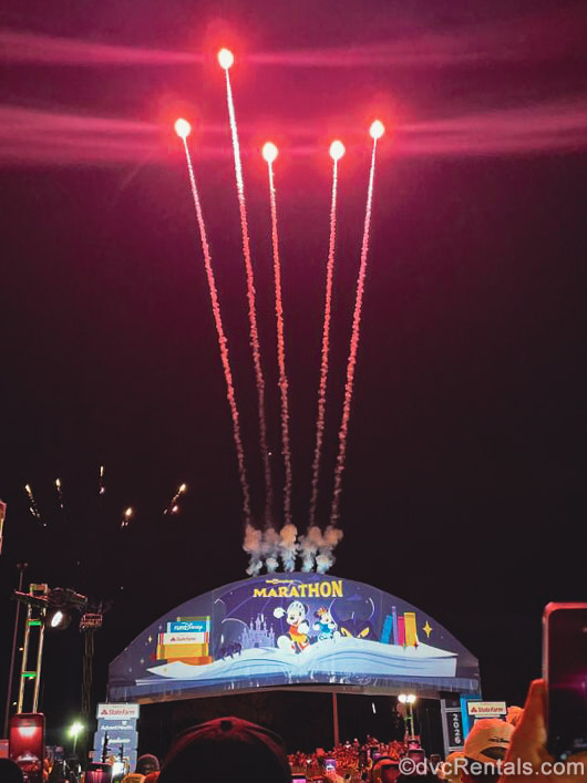 Red fireworks stream into the night sky over the starting line for a runDisney race during the Walt Disney World Marathon Weekend.