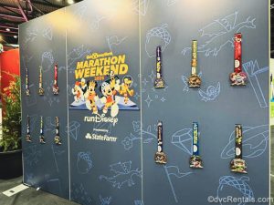 A large blue sign reading “Walt Disney World Marathon Weekend 2026” in yellow lettering displays the multi-colored race event medals.