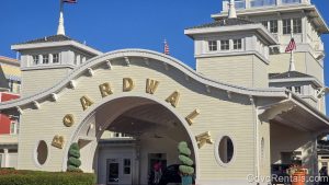 The light yellow and white exterior of Disney’s BoardWalk Villas is seen under a sunny sky. The word “Boardwalk” is spelled out in golden letters above the curved entry way.