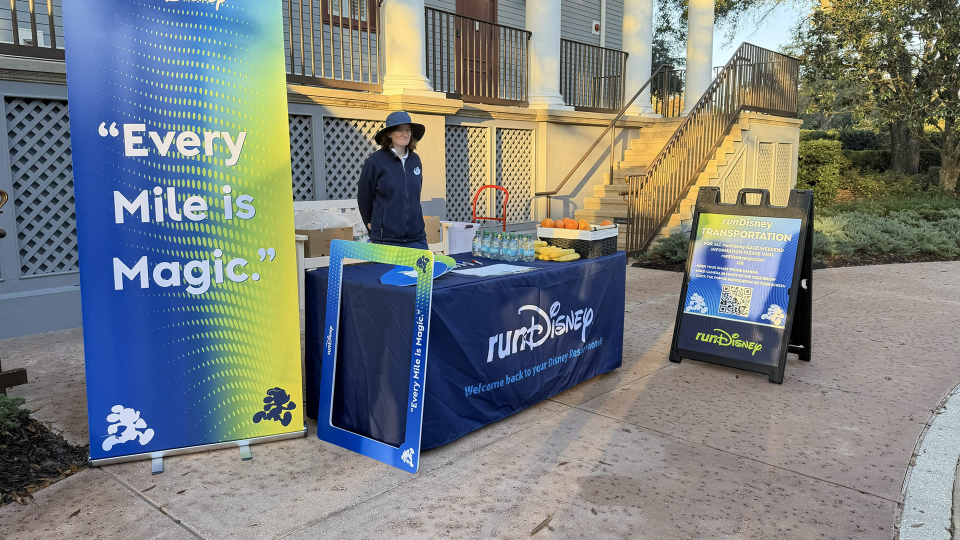 A Disney Cast Member with race event information, fruit, bottled water and themed photo props awaits runDisney participants at Disney’s Saratoga Springs Resort & Spa.