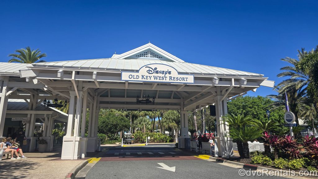 A white sign reading “Disney’s Old Key West Resort” in blue lettering hangs over the drive-up entry to the resort at Walt Disney World.