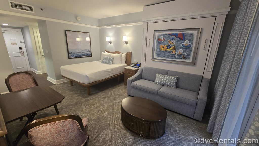 The interior of a Deluxe Studio Resort View at Disney’s Beach Club Villas. The room is decorated in shades of soft blue and gray, with Donald Duck and seaside-inspired accessories and art.