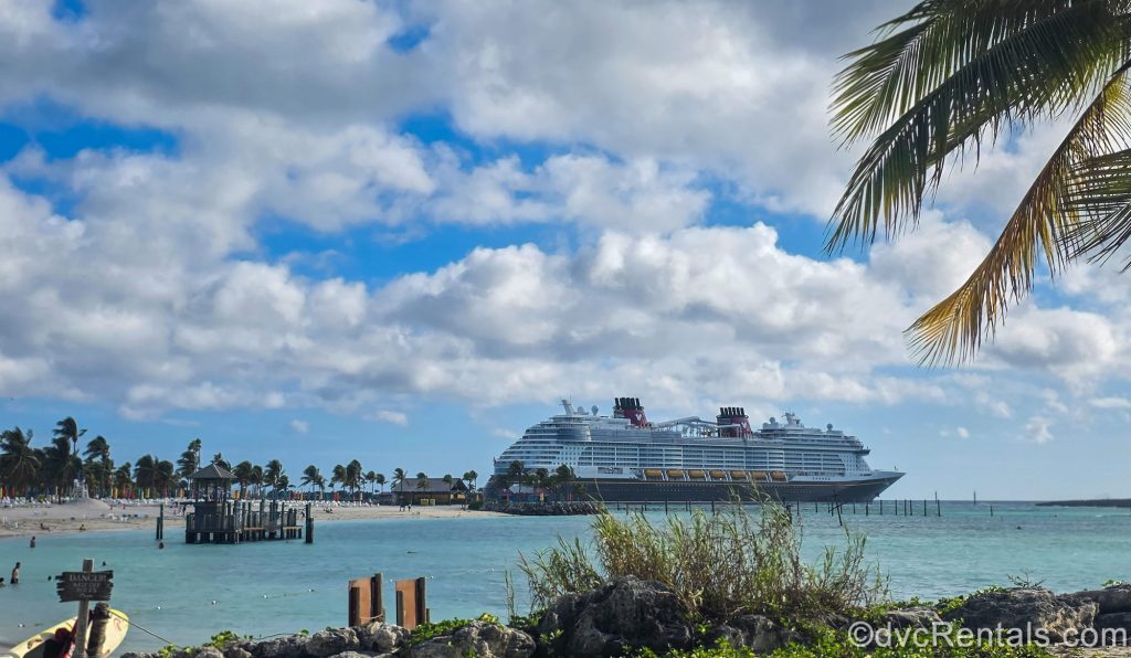 The Disney Destiny cruise ship is seen from across the beach under a blue sky as it’s docked at Disney Castaway Cay.