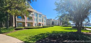 The pastel-colored exterior buildings of Disney’s Saratoga Springs Resort & Spa are seen along a walking path under a sunny blue sky.