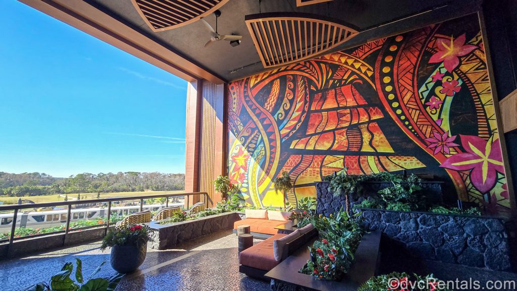 The exclusive Lava Rock Terrance for guests staying in the Island Tower of Disney’s Polynesian Villas & Bungalows. The terrace features colorful murals on the walls, lots of seating, green foliage, and views of the monorail.