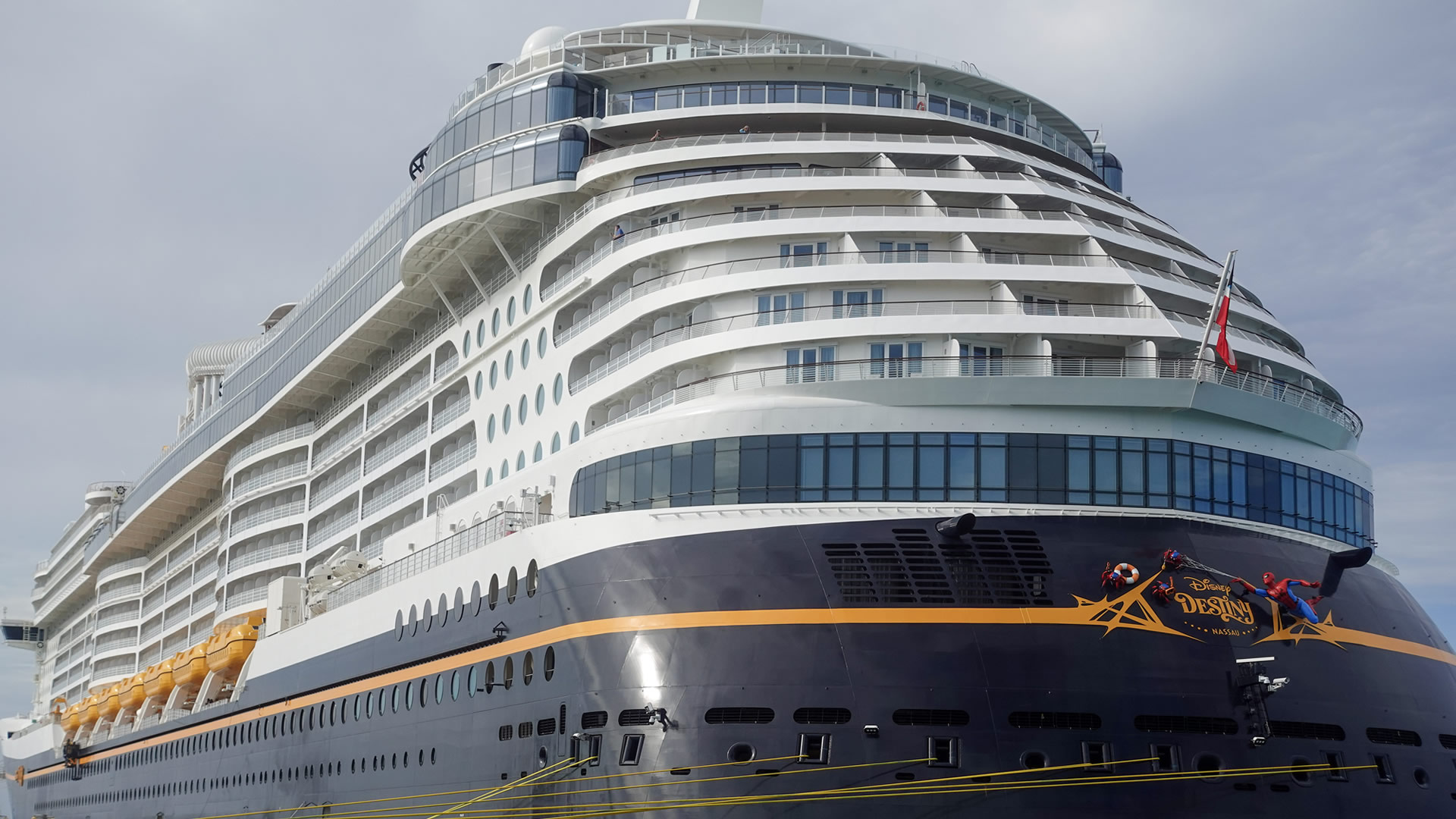 The white and blue exterior of the Disney Destiny is seen docked under a hazy sky.