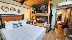 The primary bedroom in the One Bedroom DVC Cabins at Disney’s Fort Wilderness Resort. Above the king bed there are wooden art pieces featuring Chip ‘n’ Dale, and Disney characters are seen in the murals behind the bunk beds on the other side of the room as well.