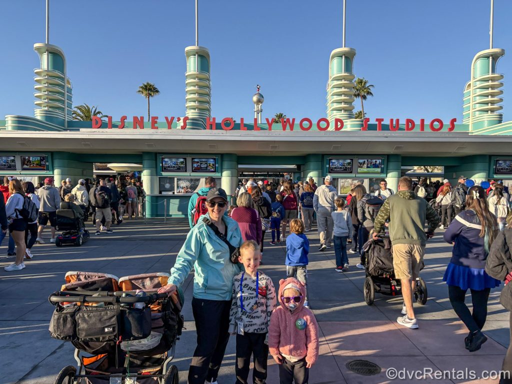 Guest blogger Christie Hecht poses with her two children under a sunny blue sky in front of the entrance to Disney’s Hollywood Studios Theme Park.