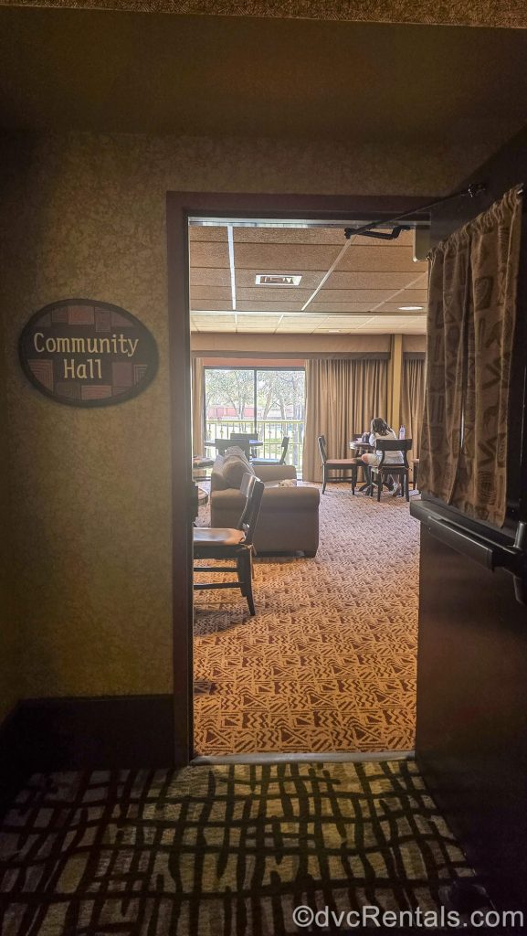 The entry to the Community Hall at Disney’s Animal Kingdom Villas Kidani Village is seen. The room is decorated with dark browns and warm tones as guests sit and enjoy activities inside.