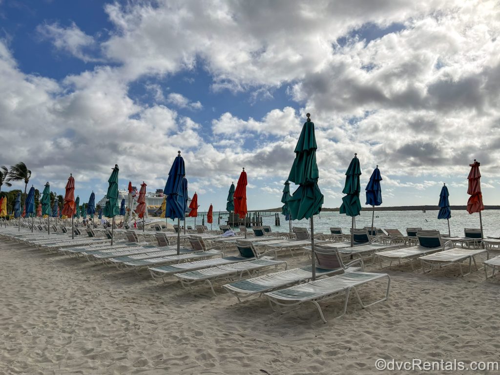 Empty white lounge chairs line the beach at Disney Castaway Cay under a blue sky.
