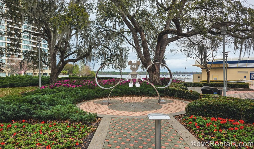 A metallic art display of Mickey Mouse is seen surrounded by green foliage and pink and red flowers at Disney’s Contemporary Resort.