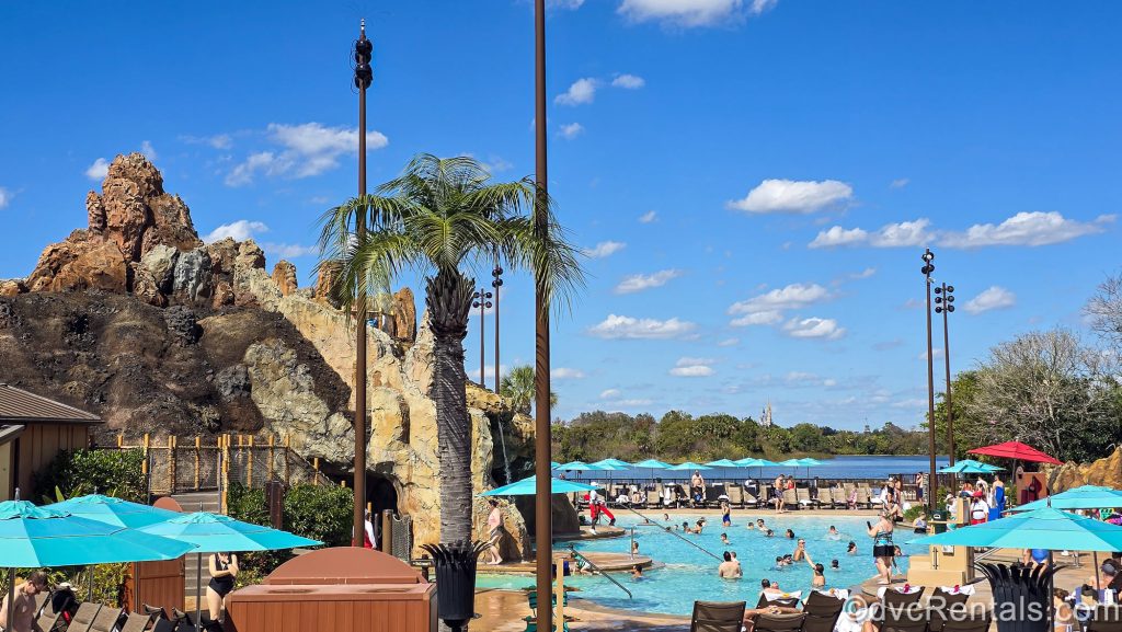 Guests enjoy the Lava Pool at Disney’s Polynesian Villas & Bungalows under a sunny blue sky with Cinderella Castle visible in the distance.