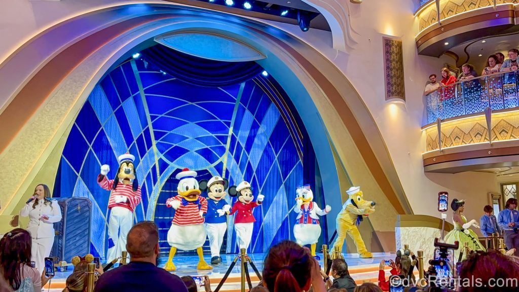 Disney characters Goofy, Donald Duck, Mickey Mouse, Minnie Mouse, Daisy Duck, and Pluto perform on stage in nautical costumes on the Grand Hall stage on the Disney Destiny.