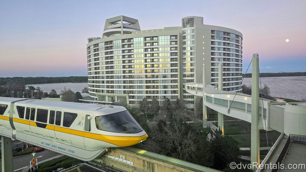 The monorail passes in front of the exterior or Bay Lake Tower at Disney’s Contemporary Resort as the sun sets over the water behind the resort.