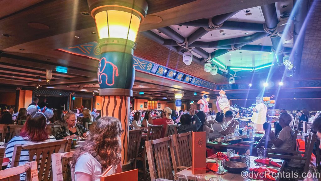 Guests enjoy dinner while watching a live performance at Pridelands: Feast of the Lion King dining room onboard the Disney Destiny.