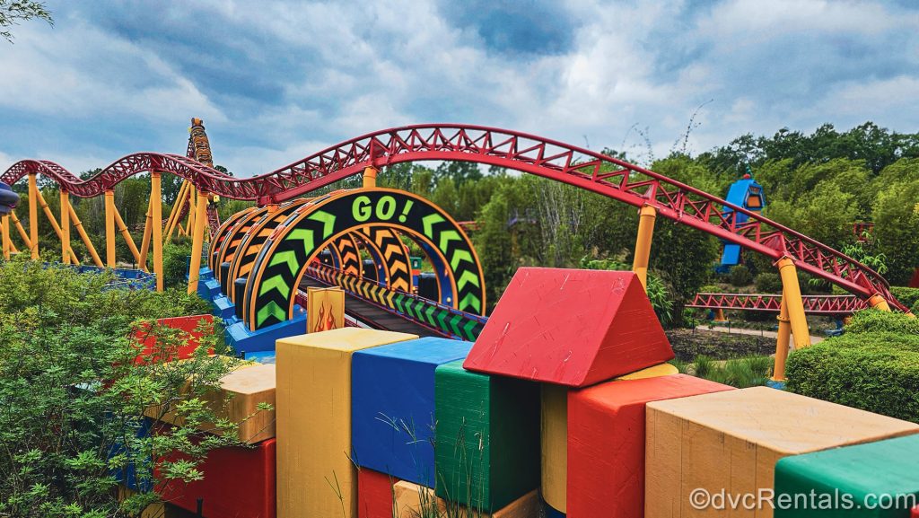 The colorful track and themed décor around Slinky Dog Dash at Hollywood Studios are seen under a cloudy sky. There is a circular sign over part of the track reading “Go!” in neon green writing.