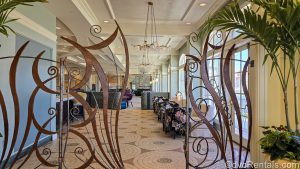 The ornate brown entry way to Citricos at Disney’s Grand Floridian Resort & Spa is seen. Elegant floral chairs and barstools can be seen in the lounge area, leading to the blue and purple Mary Poppins Returns-themed dining room.