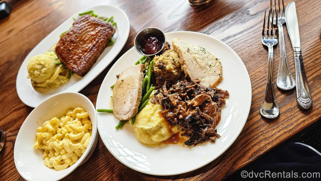 Thanksgiving-inspired foods like turkey, mashed potatoes, stuffing, and meatless meatloaf are seen served on white plates at Liberty Tree Tavern at the Magic Kingdom.