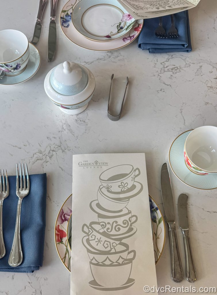 A white menu decorated with teacups and reading “The Garden View Lounge” is seen in the table setting for the afternoon Tea Experience at Disney’s Grand Floridian Resort & Spa.
