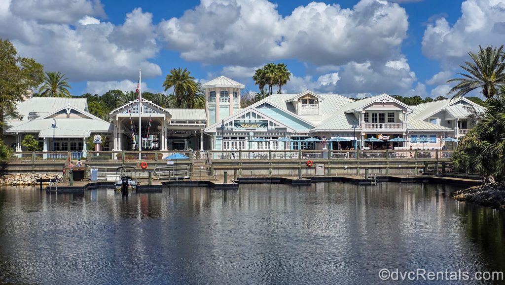 Hospitality House at Disney’s Old Key West Resort is seen from across the water under a blue sky. Palm trees are seen in the landscaping.