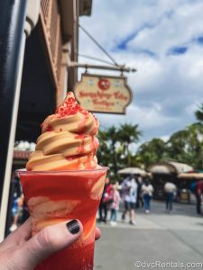 A hand holds up an “I Lava You” float made with orange Dole Whip at Sunshine Tree Terrace at Magic Kingdom. Red popping candies can be seen on top of the frozen treat.