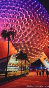 Spaceship Earth is illuminated with shades of pink, purple, and orange under a night sky as guests make their way to the park’s exit.