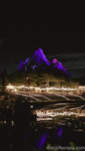 Expedition Everest is illuminated with purple light under a dark night sky as warm white lights glow around Disney’s Animal Kingdom Theme Park.