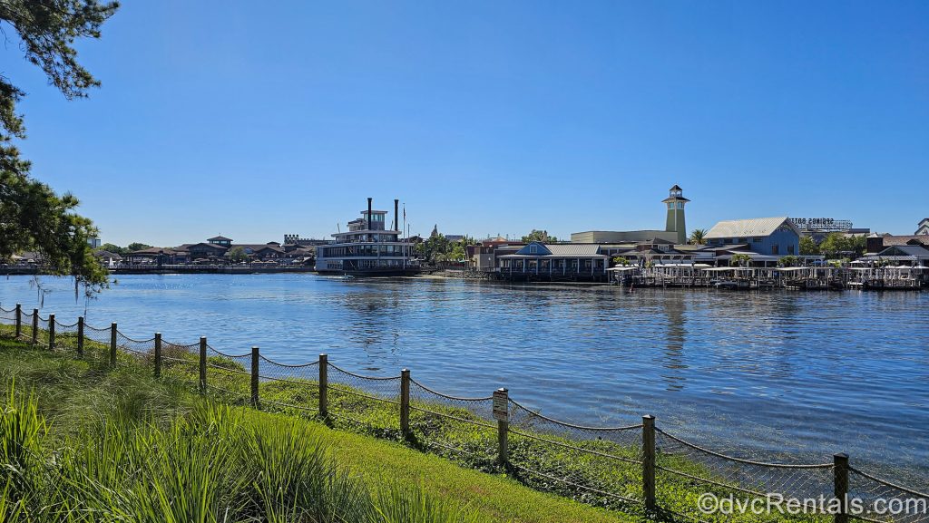 Restaurants and shops at Disney Springs are seen across the water from Disney’s Saratoga Springs Resort & Spa under a blue sky.