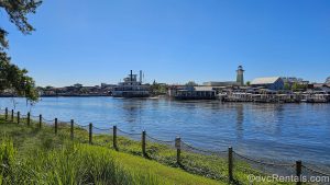 Restaurants and shops at Disney Springs are seen across the water from Disney’s Saratoga Springs Resort & Spa under a blue sky.