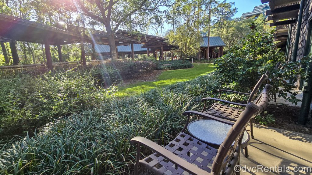 Two brown chairs are seen on a private patio at the Boulder Ridge Villas at Disney’s Wilderness Lodge as the sun sparkles through the trees during golden hour.