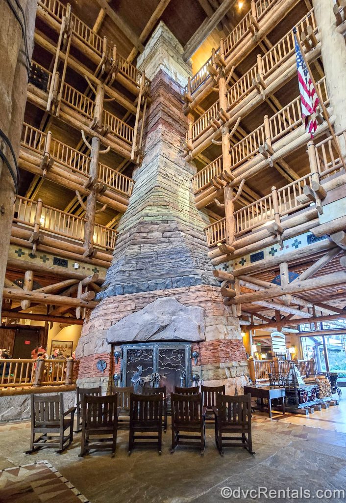 Dark wooden rocking chairs are gathered in front of the large stone fireplace in the lobby of Disney’s Wilderness Lodge.