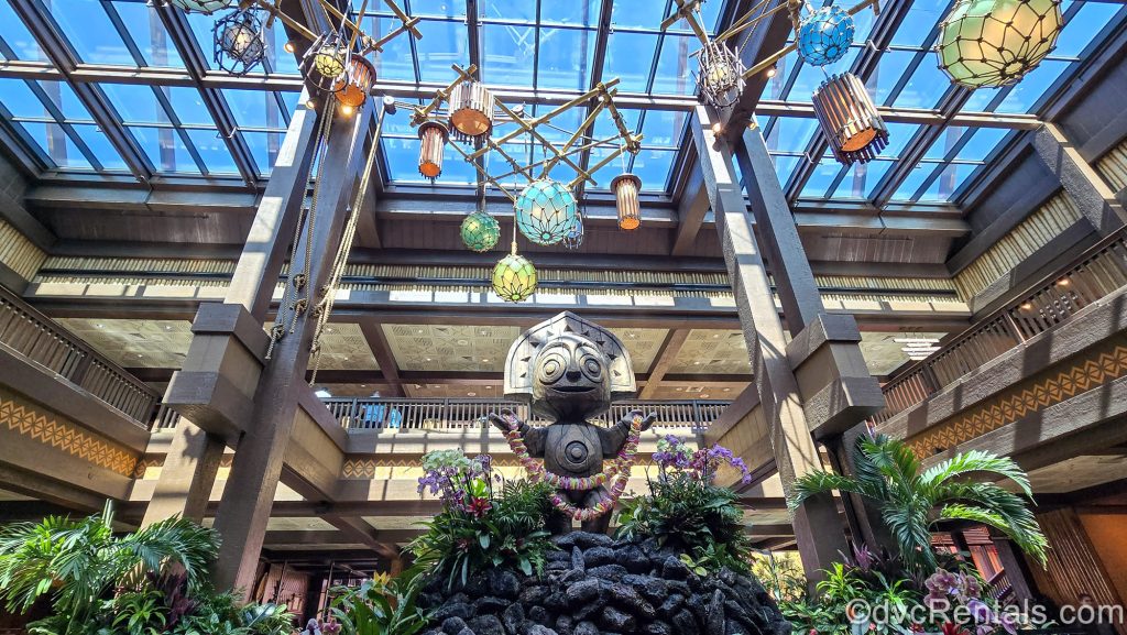A wooden Tiki statue is seen in the main lobby of Disney’s Polynesian Villas & Bungalows. The dark woods in the resort’s décor can been seen along with green foliage, and brightly colored lanterns hanging from the glass ceiling.