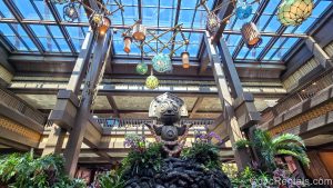 A wooden Tiki statue is seen in the main lobby of Disney’s Polynesian Villas & Bungalows. The dark woods in the resort’s décor can been seen along with green foliage, and brightly colored lanterns hanging from the glass ceiling.