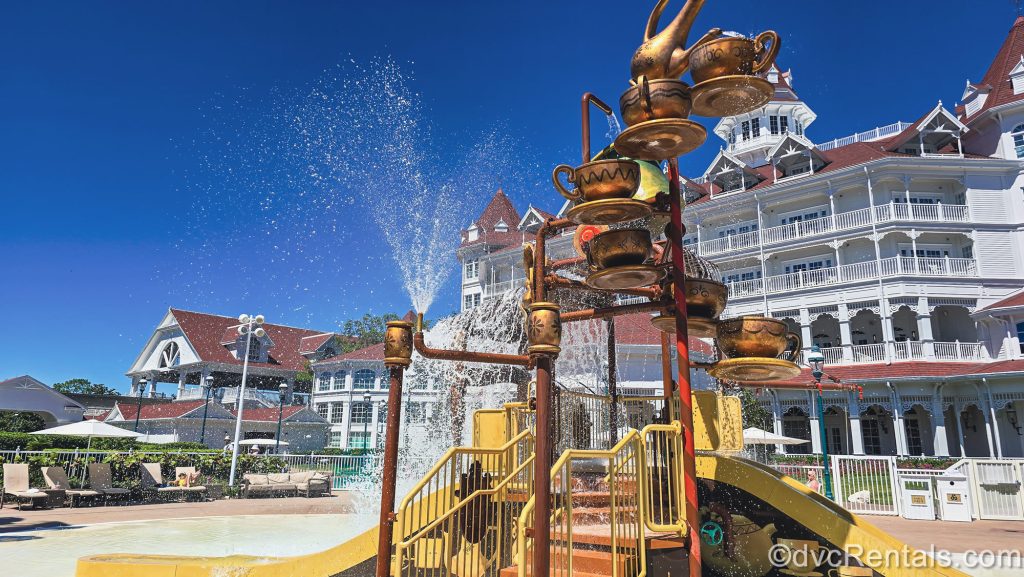 Splashes of water sparkle under a blue sky as guests enjoy the Alice in Wonderland-themed water play area at Disney’s Grand Floridian Resort & Spa.